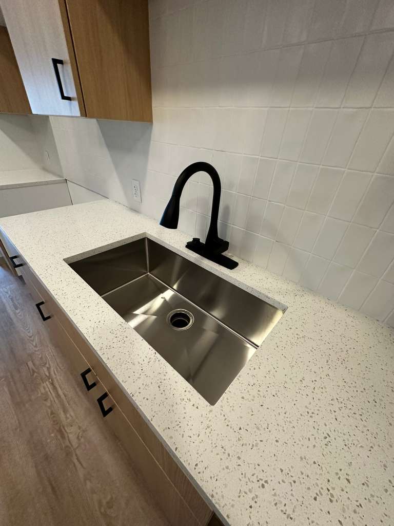 Spotless kitchen sink and quartz countertop with modern black fixtures cleaned by Stellar Cleaning Services SWFL